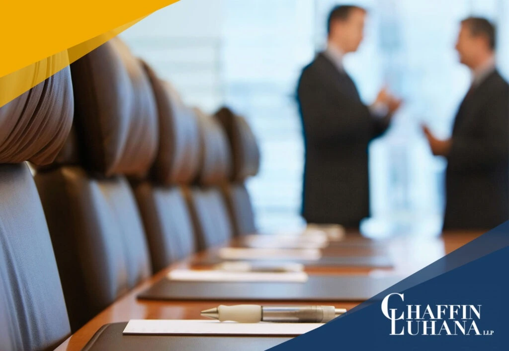 Conference room with leather chairs and documents on the table, two business professionals talking in the background.