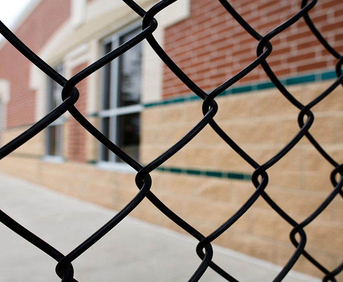 A close-up view of a chain-link fence in front of a school building, symbolizing barriers to safety and accountability in institutions.
