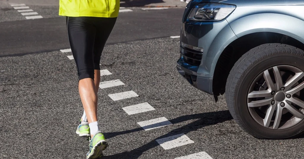 Pedestrian jogging across a crosswalk as a car approaches the intersection.