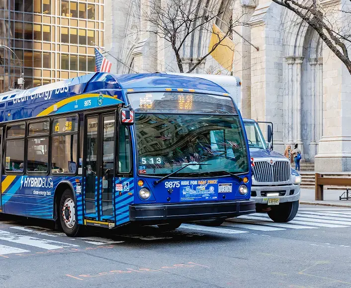 A blue city bus driving through an urban intersection, representing public transportation and bus accident awareness.