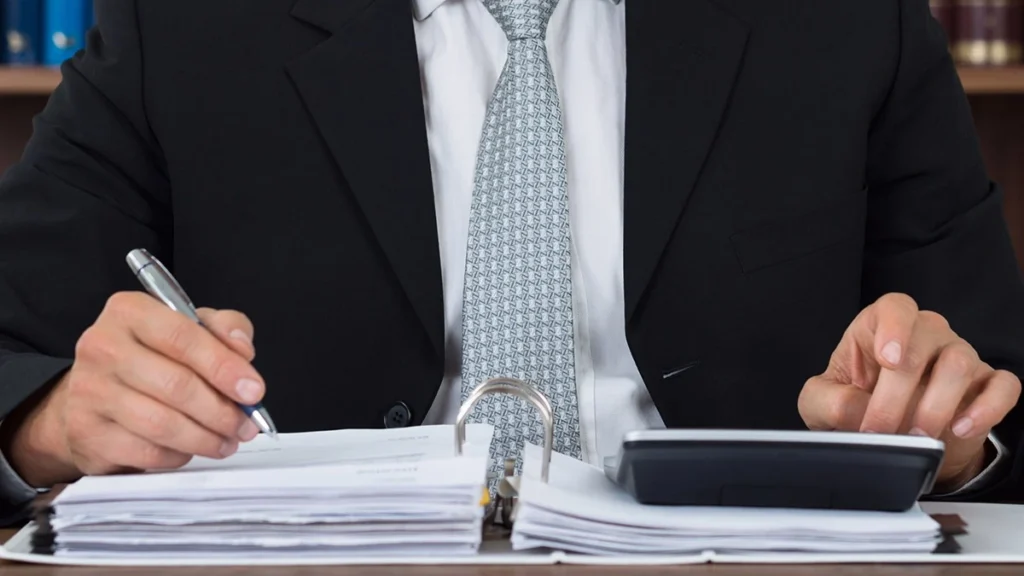 Personal injury lawyer in a suit reviewing paperwork and using a calculator at a desk.