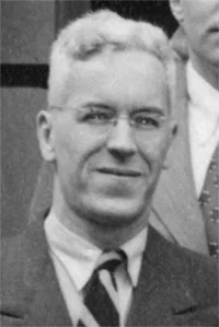 Black-and-white portrait of an older man wearing glasses, a suit, and a tie.