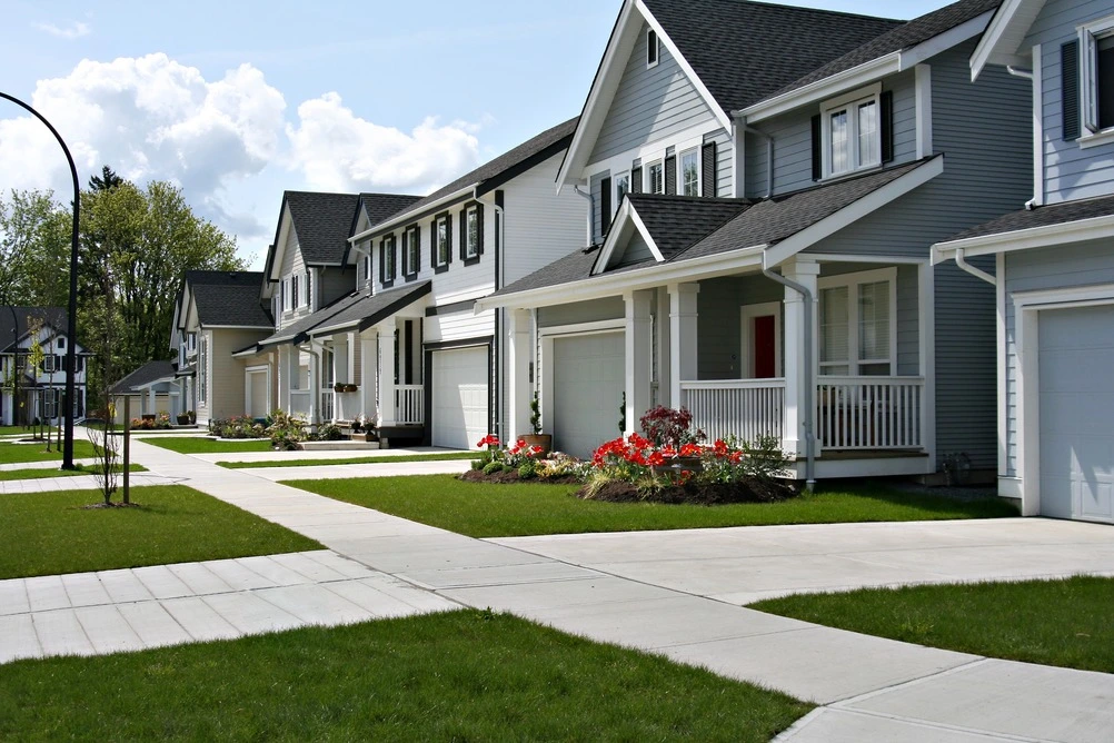 Row of modern suburban houses with well-kept lawns and sidewalks on a quiet residential street.